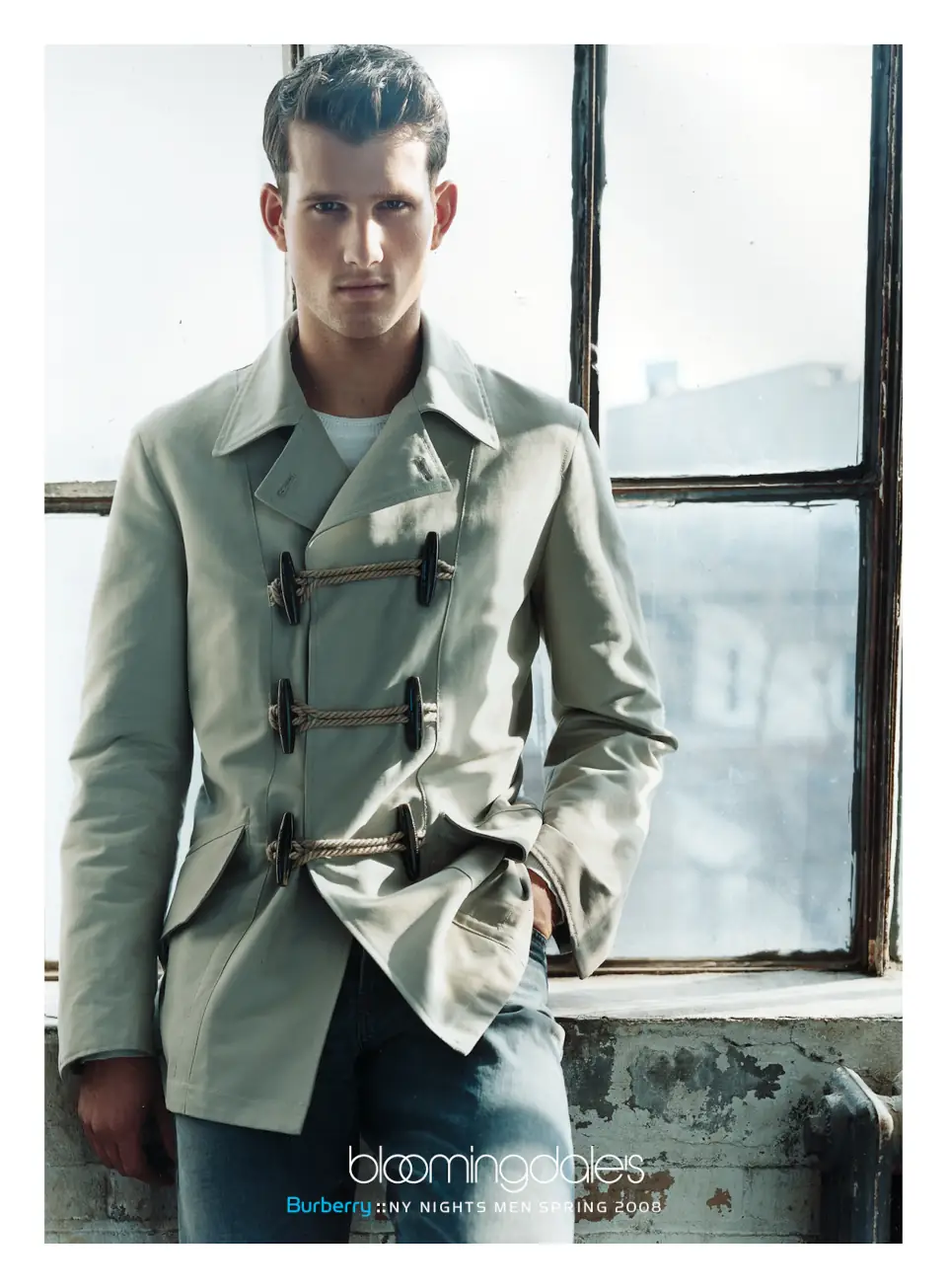 A male model wearing a Burberry light jacket standing by a large industrial window. Campaign by PlanetFab Studio.