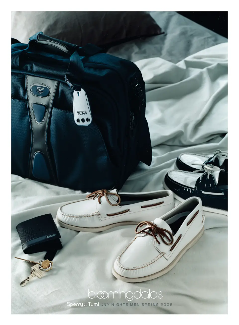 A Tumi travel bag and Sperry boat shoes are displayed on a white bed. Campaign by PlanetFab Studio