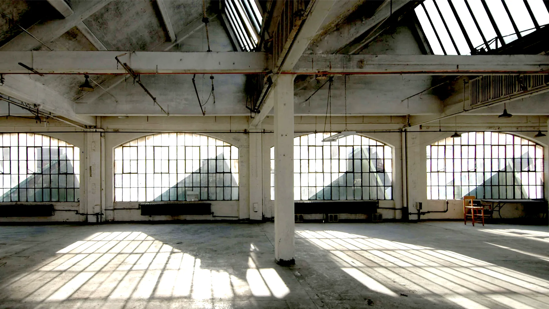 Large industrial space with skylight windows and dramatic lighting casting shadows. Campaign by PlanetFab Studio.